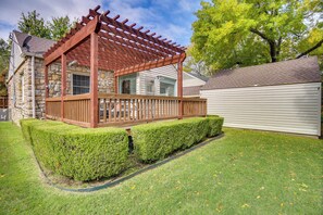 A wooden deck with a pergola, stone house, and well-maintained lawn.