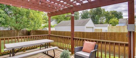 A covered outdoor patio with a picnic table, wicker furniture, and a potted plant.
