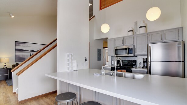 A modern kitchen with a large island, stainless steel appliances, and bar stools. - Balcony & Ski Slope Views: Idyllic Granby Condo! (Granby)