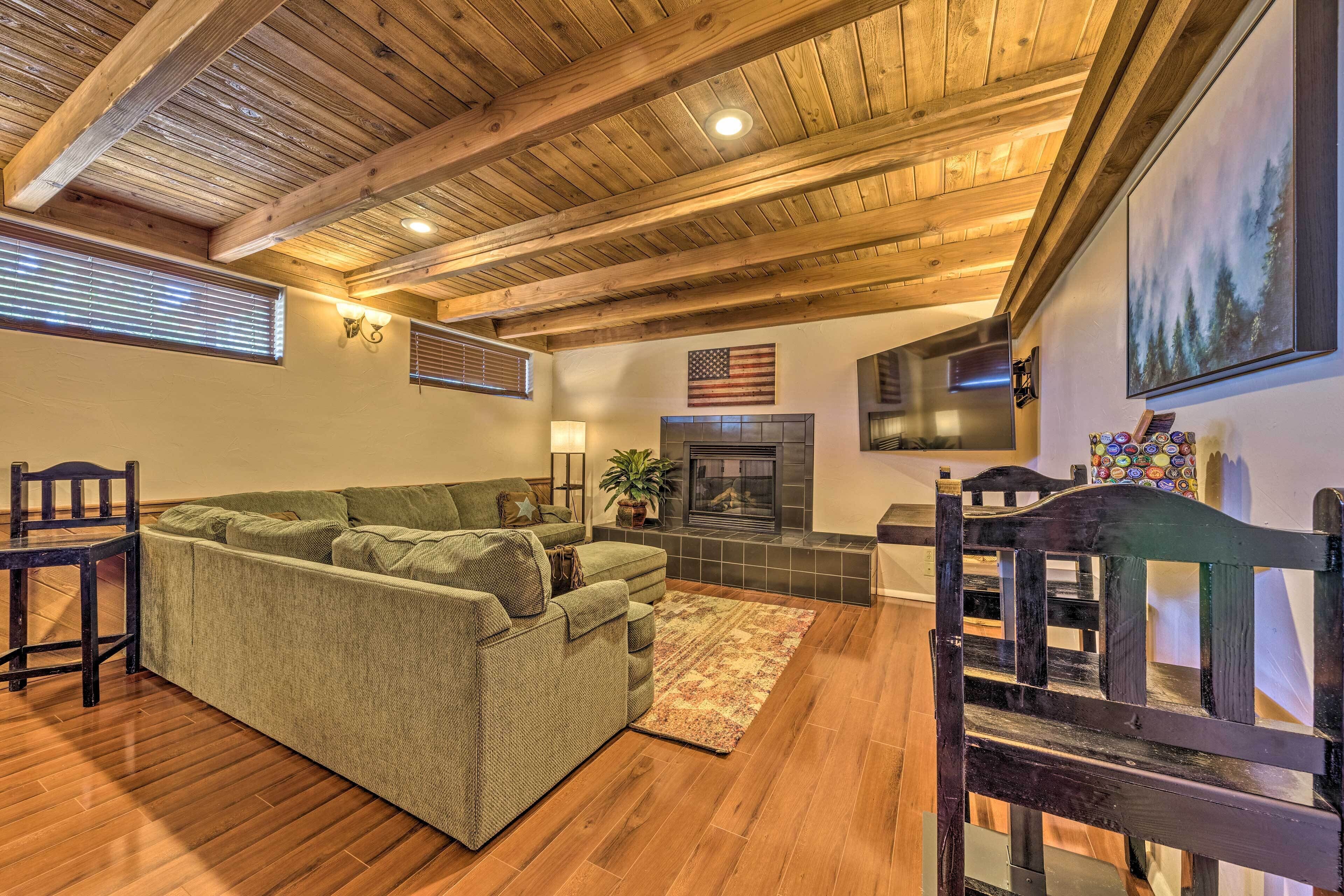A cozy living room with a green sofa, wooden flooring, a fireplace, and a ceiling with exposed beams.