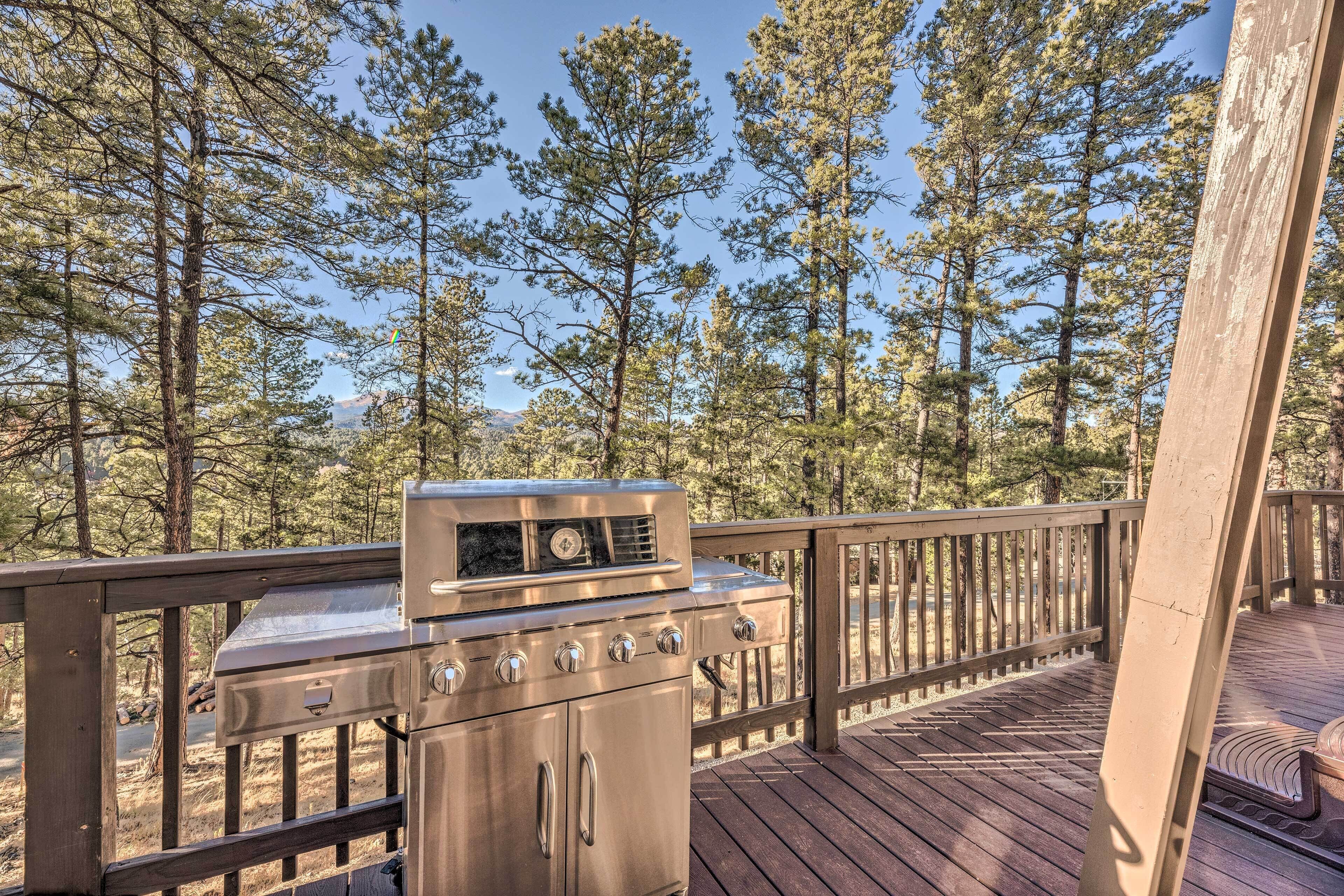 A deck with a stainless steel grill, surrounded by a wooden railing and overlooking a forested area.