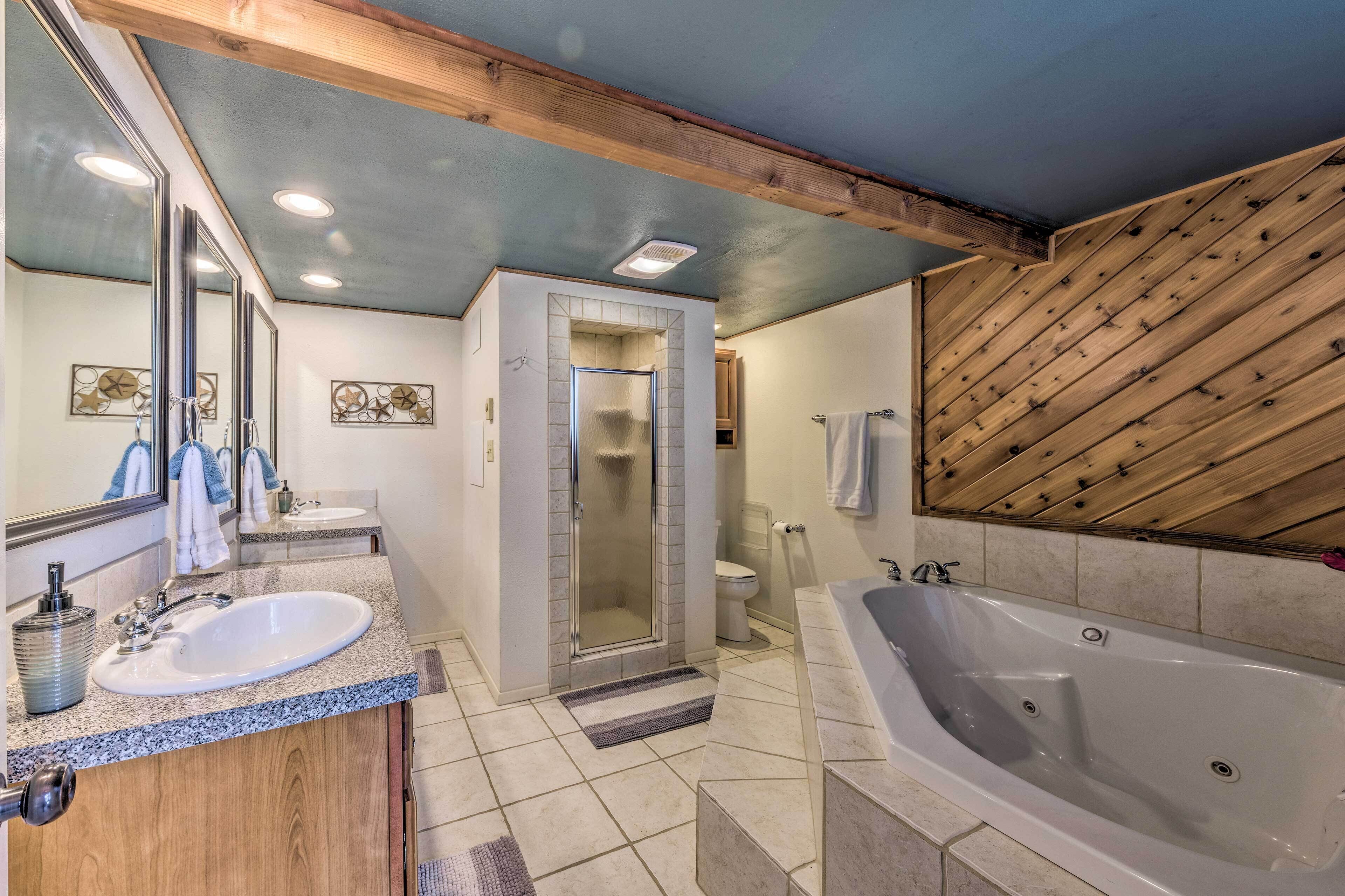 A bathroom with a large bathtub, a sink, a shower, and wooden ceiling beams.