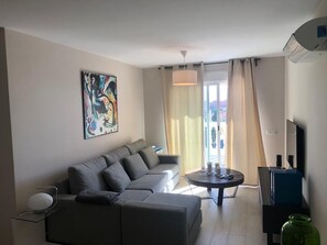 Un salon moderne avec un canapé d’angle gris, une table basse ronde et un téléviseur à écran plat posé sur un meuble noir.
