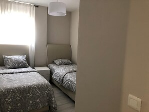 Une chambre avec deux lits, une table de chevet, une lampe et une fenêtre avec des rideaux.