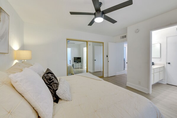 A bedroom with a bed, a ceiling fan, a mirror, and a bathroom visible through an open door.