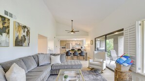 A modern living room with a grey sectional sofa, a glass coffee table, and a dining area with a kitchen in the background. - Quiet Palm Desert Condo: Workspace & Pool Access! (Palm Desert)