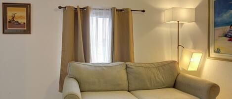 Un canapé beige dans une pièce avec une fenêtre, une lampe et deux tableaux encadrés accrochés aux murs.