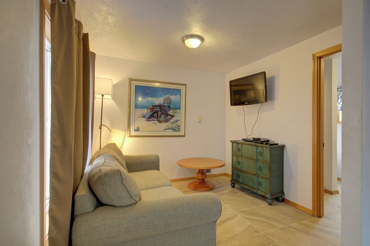A living room with a sofa, a round table, a green dresser, a painting on the wall, and a TV mounted on the wall.
