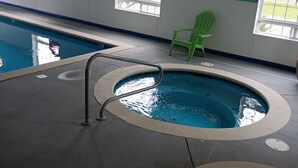 An indoor swimming pool with a safety sign, a green chair, and a view of the outside. - The Westerly Motel (Ocean Shores)