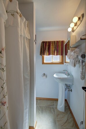 A bathroom with a white sink, a window with striped curtains, a towel rack, and a shower curtain. - The Westerly Motel (Ocean Shores)
