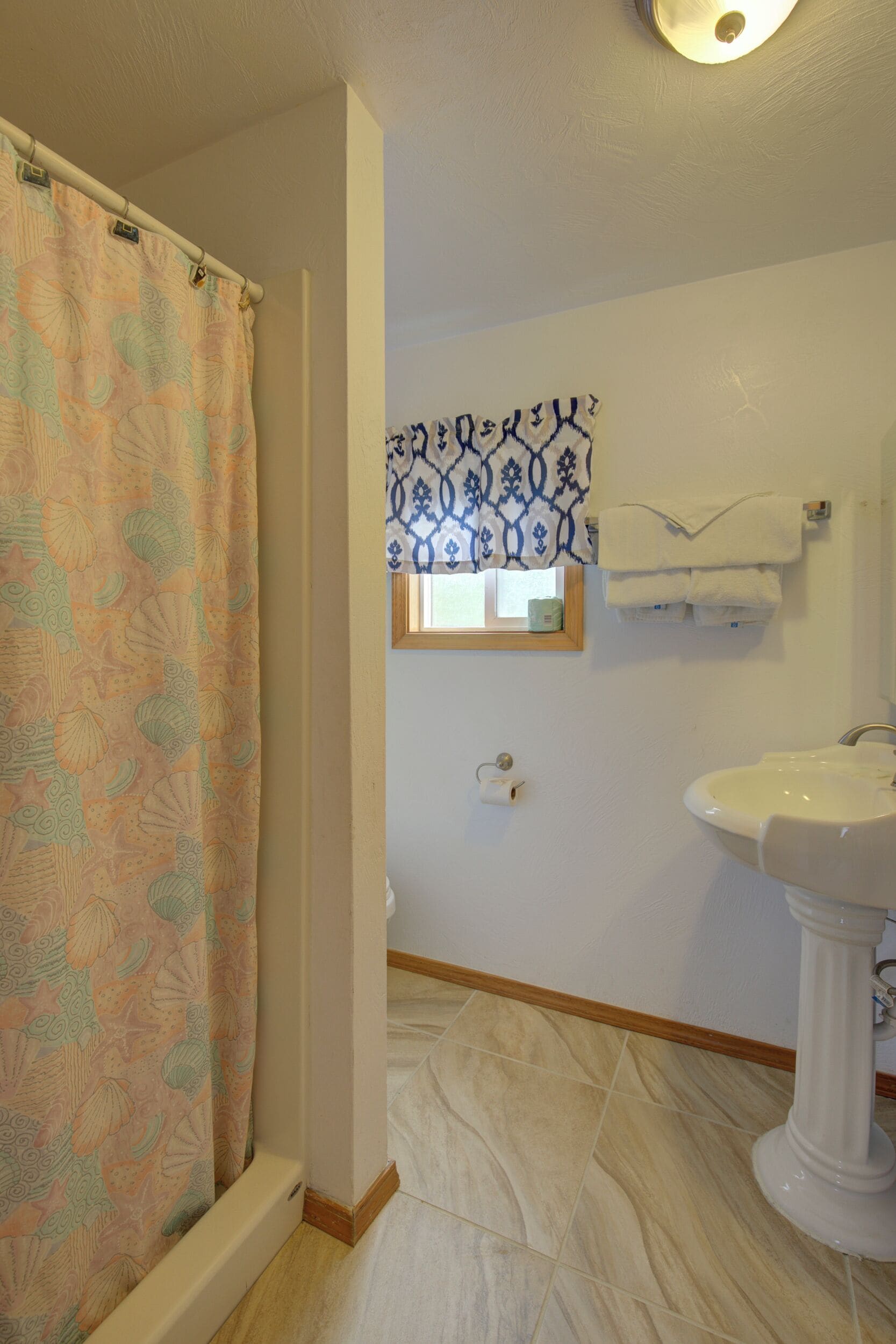 A bathroom with a shower curtain, a sink, and a window with patterned curtains.