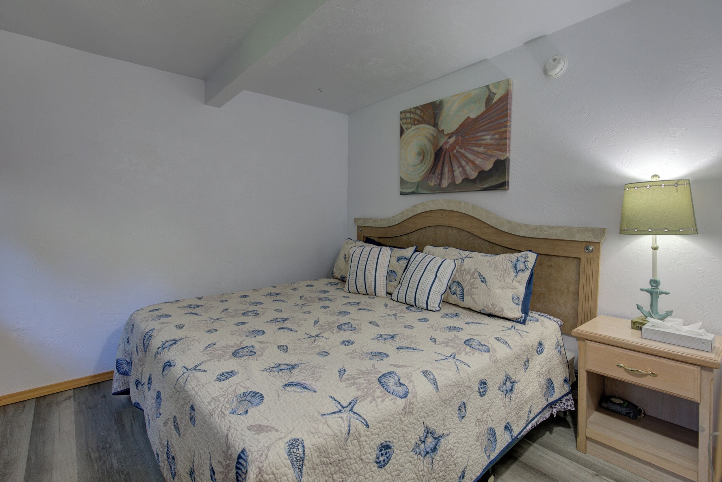 A bedroom with a bed, a nightstand, a lamp, and a painting on the wall.