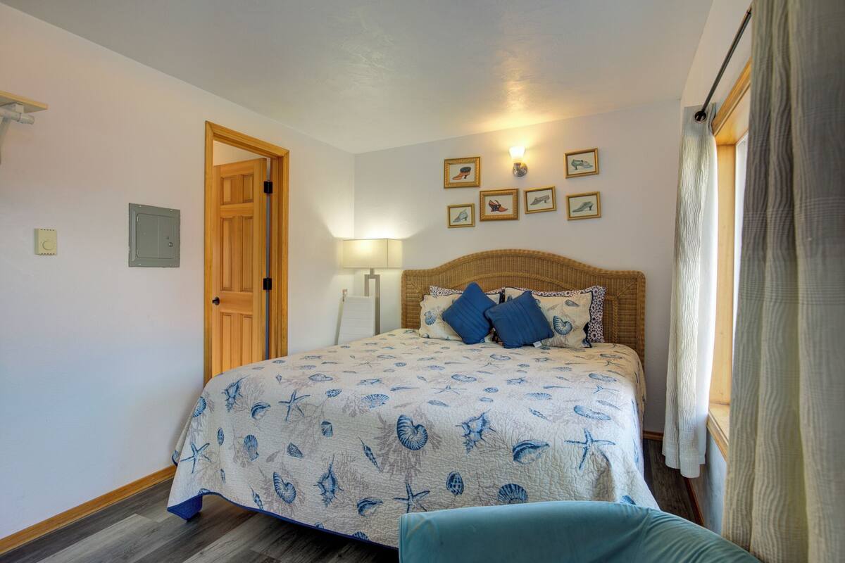 A bedroom with a bed, a wooden door, a wall-mounted lamp, and framed pictures.