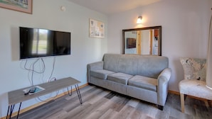 A living room with a grey sofa, a wooden coffee table, a flat-screen TV mounted on the wall, a framed picture, and a mirror. - The Westerly Motel (Ocean Shores)