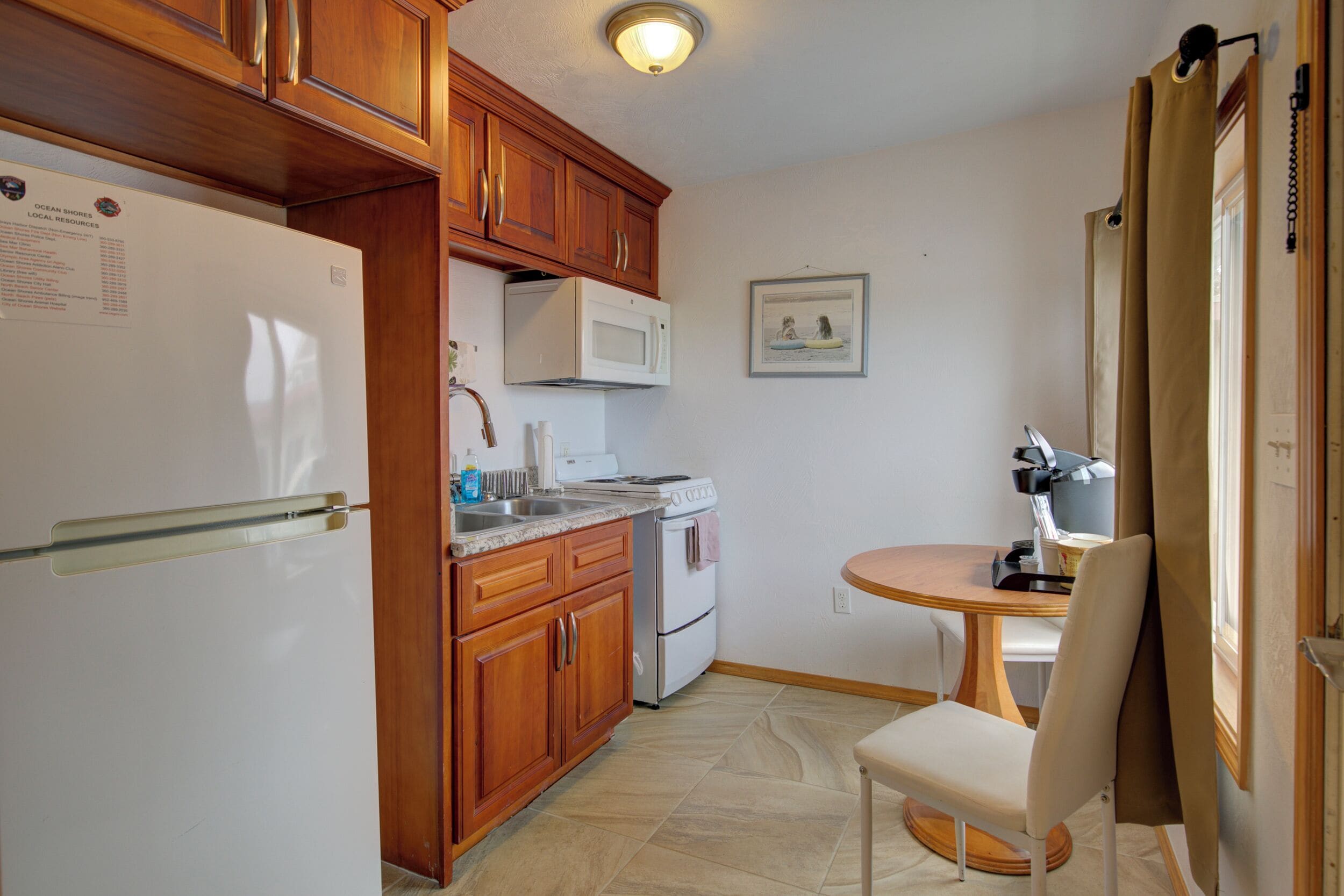 Une cuisine avec des meubles en bois, un réfrigérateur blanc, un four à micro-ondes, une cuisinière et une table à manger avec une chaise.