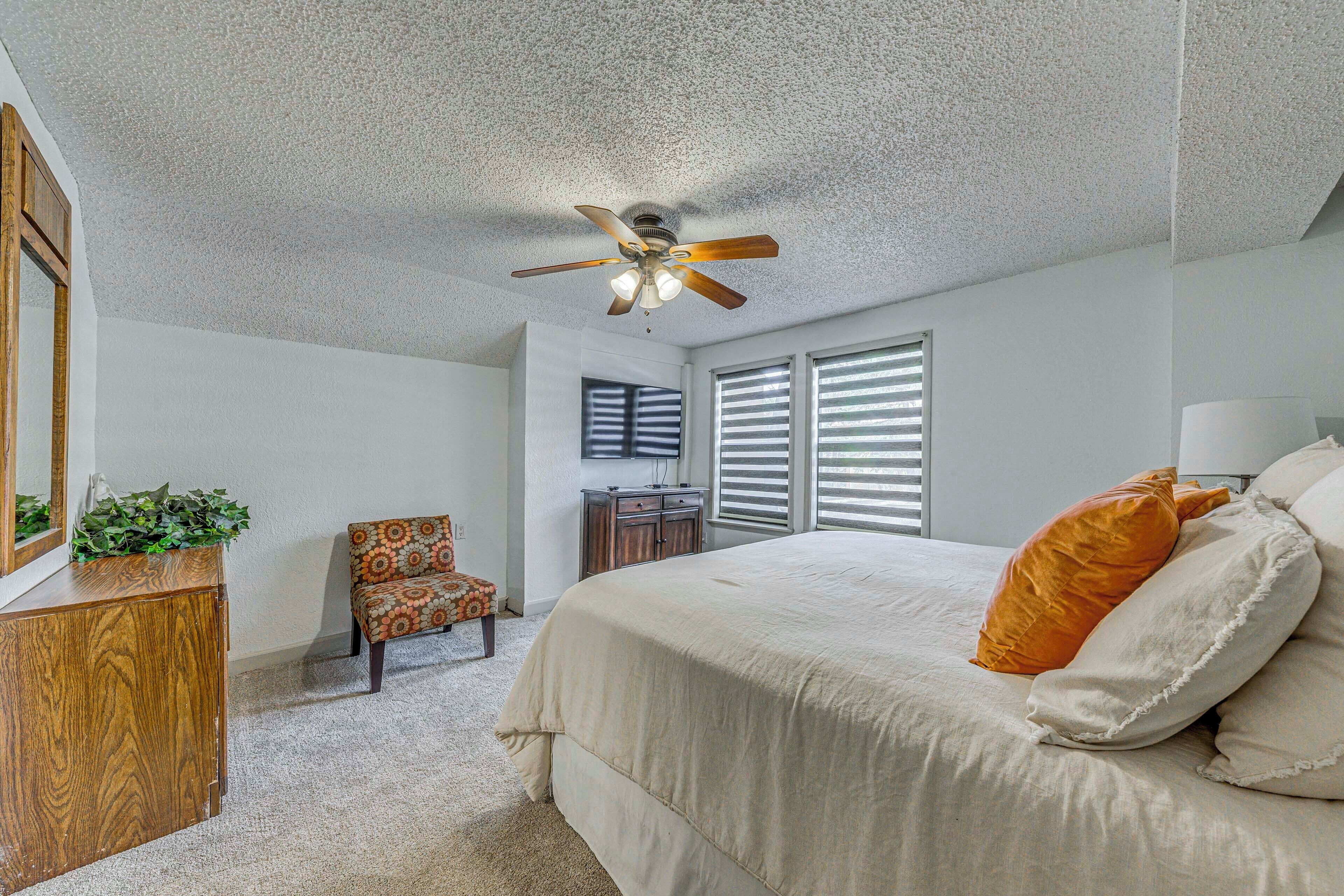 A bedroom with a bed, a ceiling fan, a dresser, a chair, and a desk.
