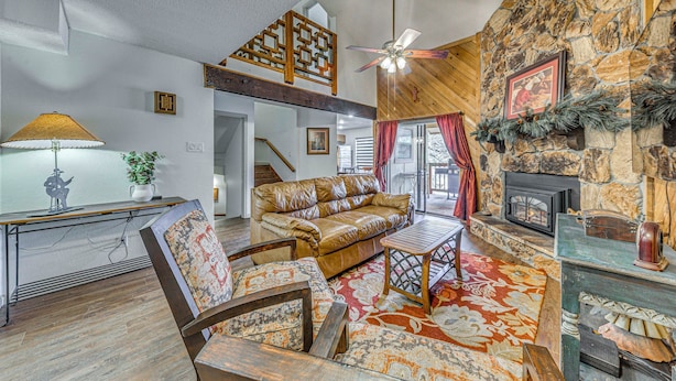 A cozy living room with a stone fireplace, a wooden ceiling fan, and a leather sofa. - Spacious Ruidoso Retreat w/ Hot Tub & 2 Kitchens! (Ruidoso)