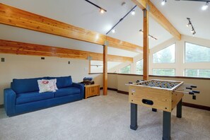 A room with a blue sofa, a foosball table, and large windows.