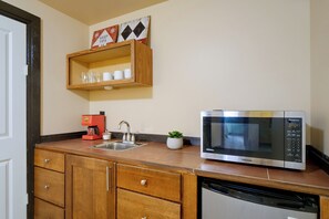 Una cocina compacta con microondas integrado, cafetera y una pequeña planta en maceta.