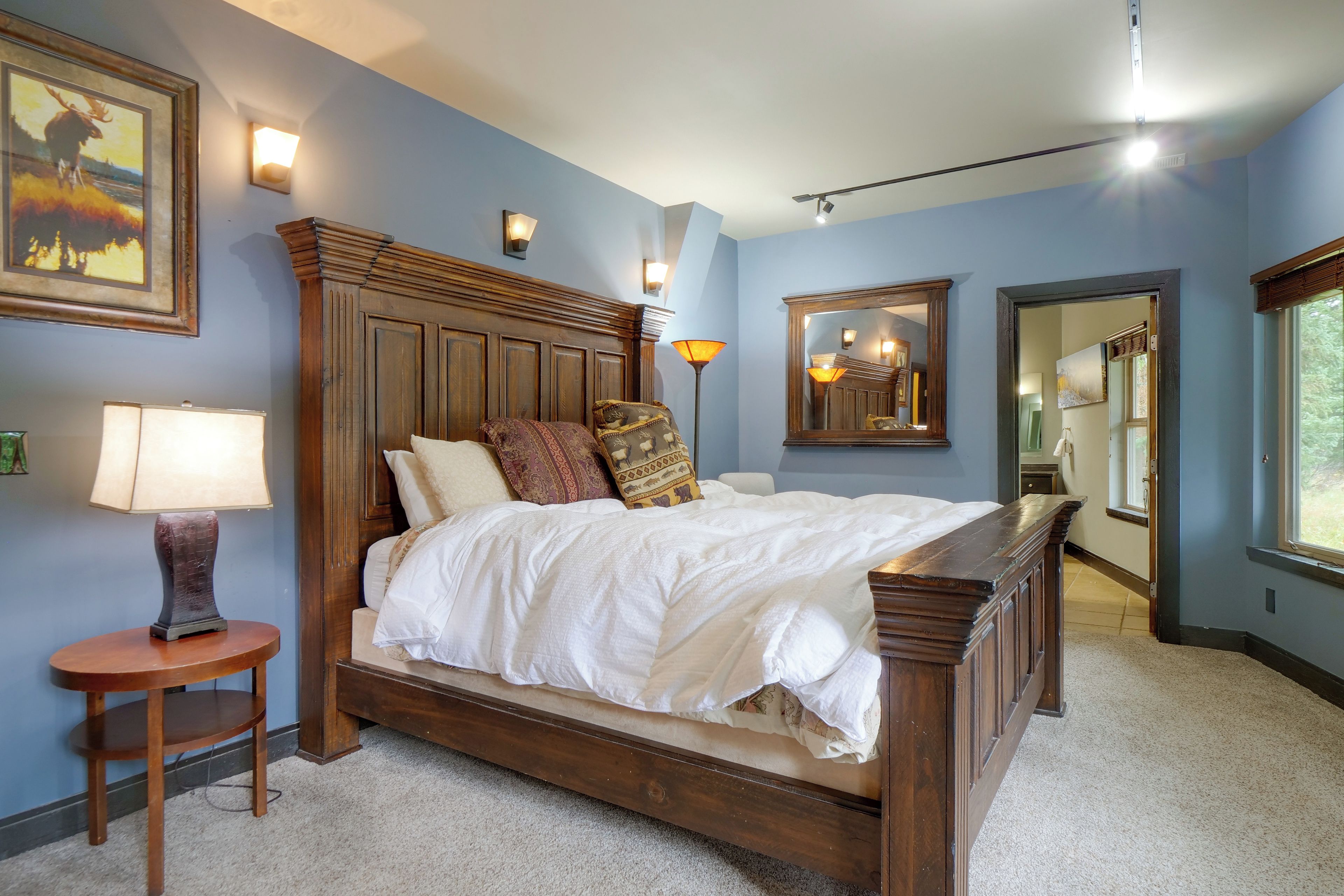 A bedroom with a large bed, a nightstand, a lamp, a mirror, and artwork on the walls.