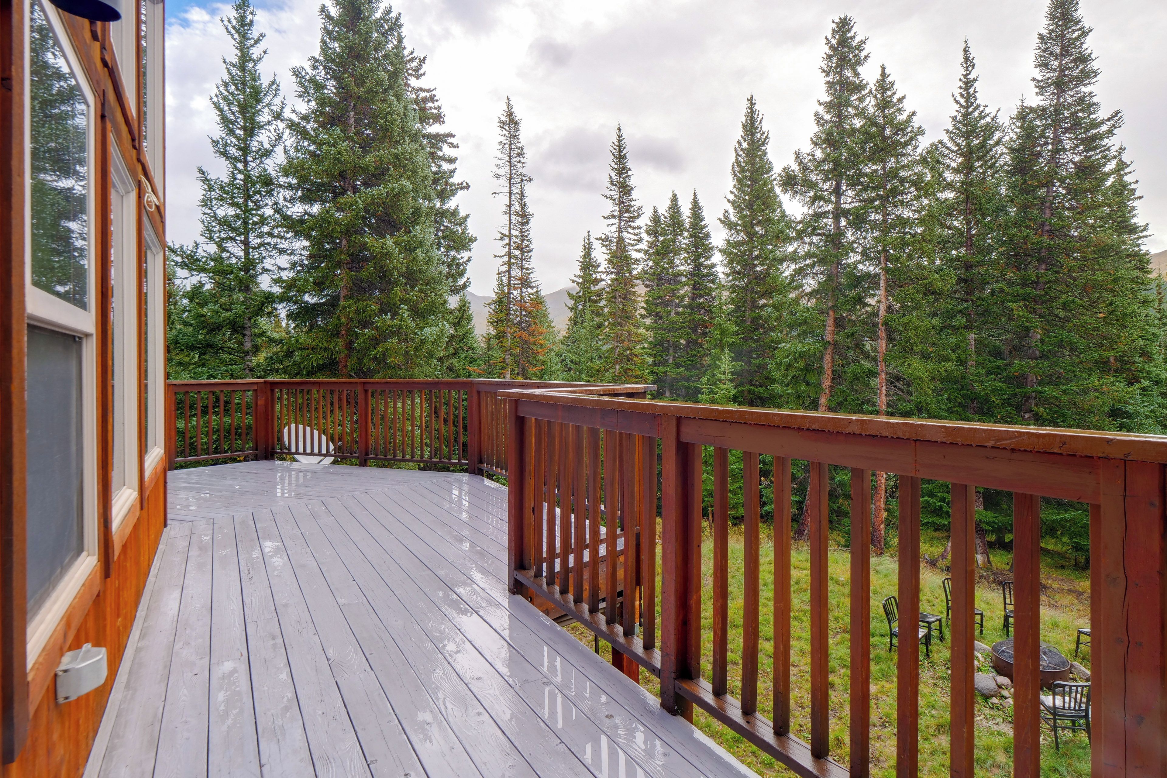 A wooden deck with a railing, overlooking a forested area with tall trees.
