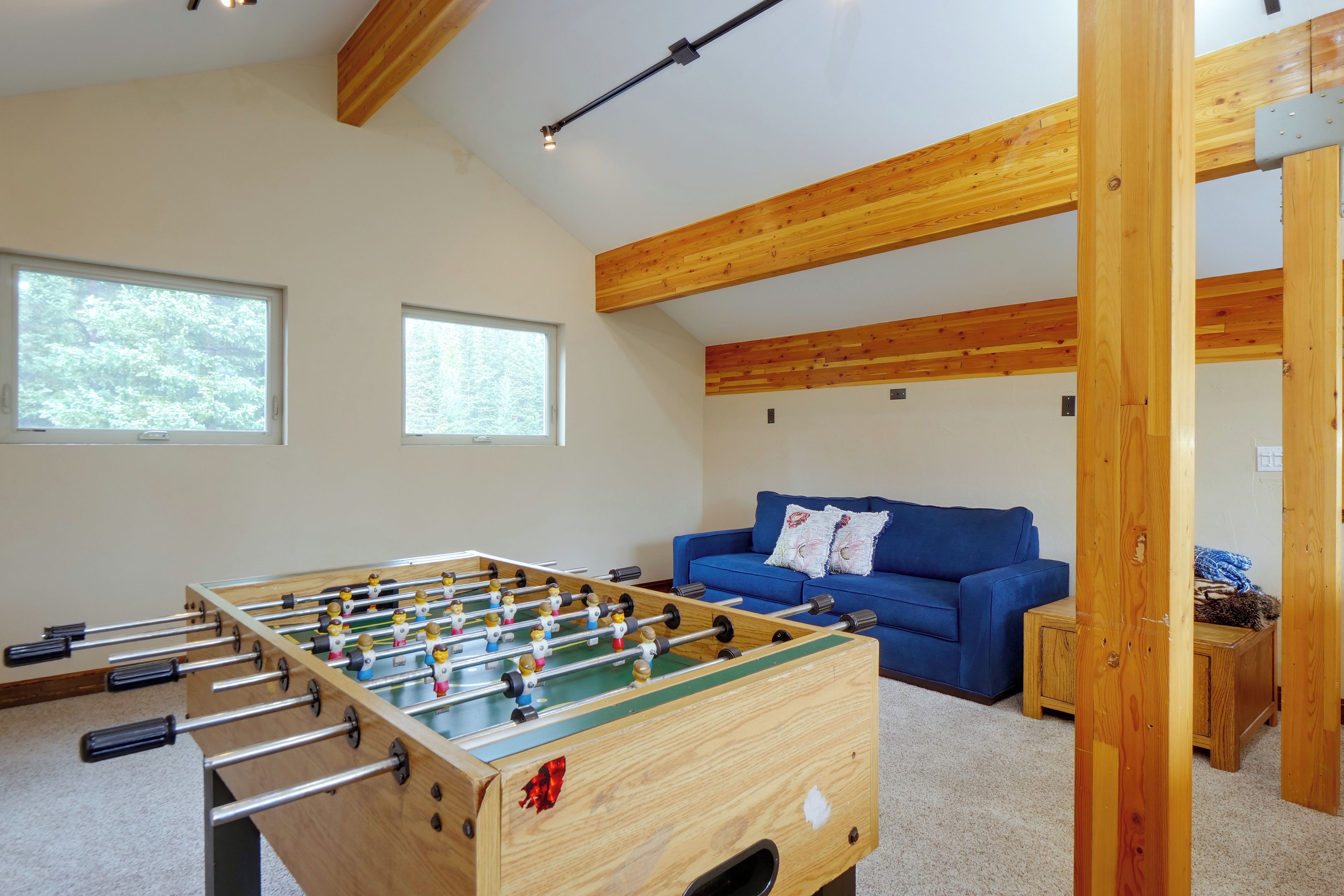A room with a foosball table, a blue sofa, and wooden beams on the ceiling.