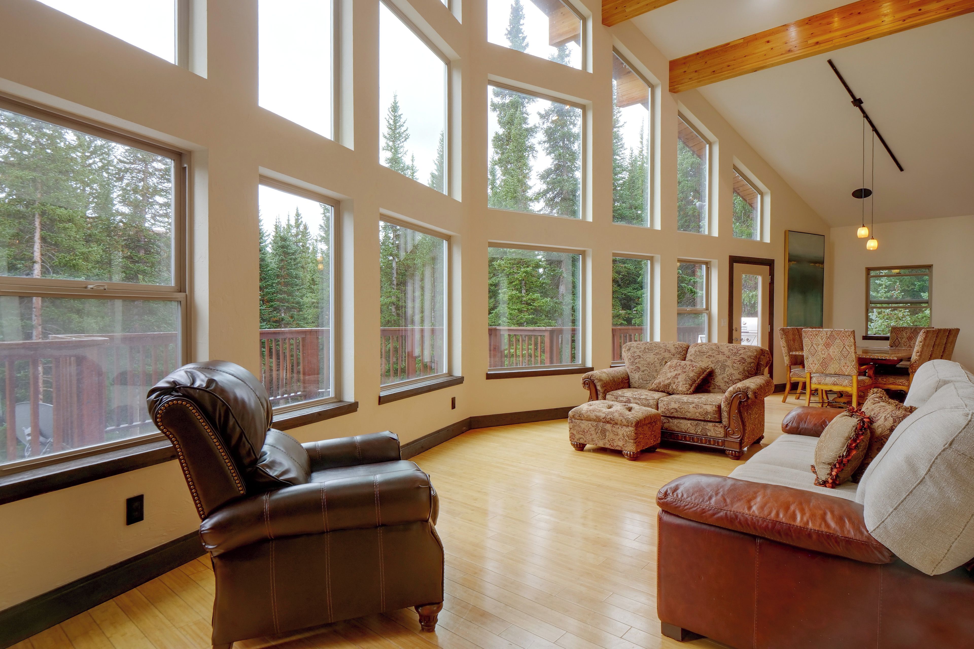 A spacious living room with large windows, a wooden ceiling, and a view of a deck.