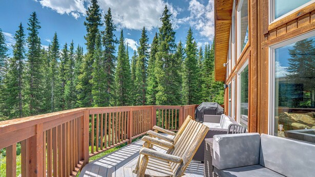 Eine Holzterrasse mit Gartenmöbeln, darunter Stühle und eine Couch, mit Blick auf ein bewaldetes Gebiet.