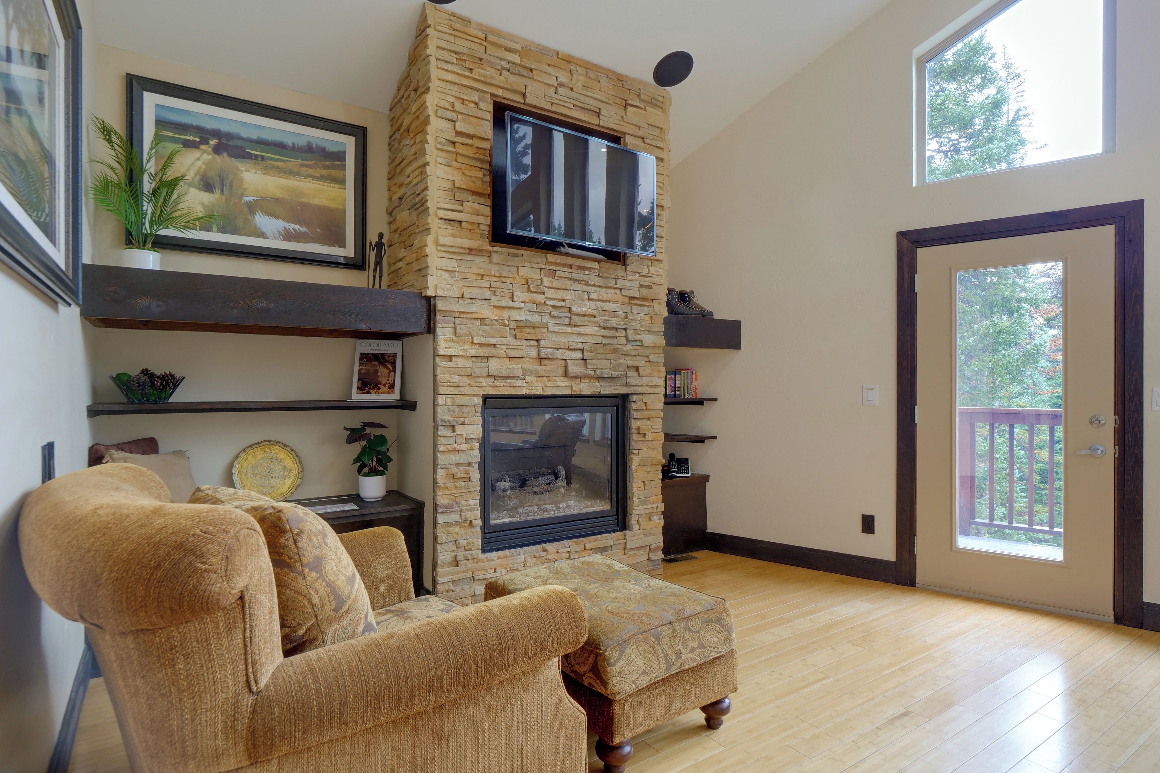 Una sala de estar con chimenea de piedra, televisor montado y un ventanal grande.