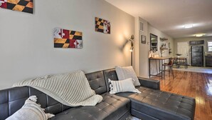 A modern living room with a dark leather sofa, a kitchen in the background, and abstract art on the walls. - Midtown Baltimore Hub Half Mi to Penn Station (Baltimore)