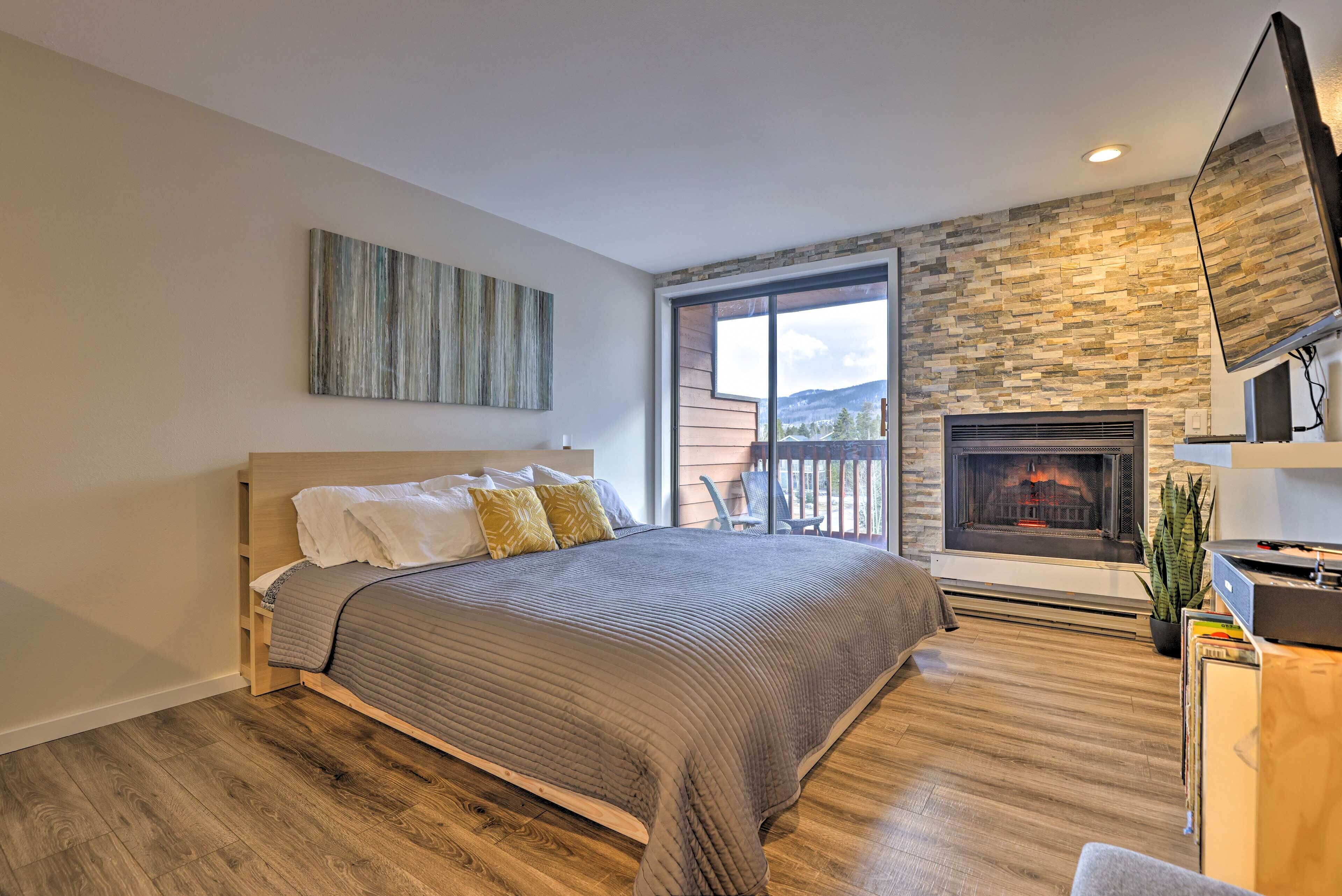 A bedroom with a large bed, a fireplace, and a view of the outdoors.