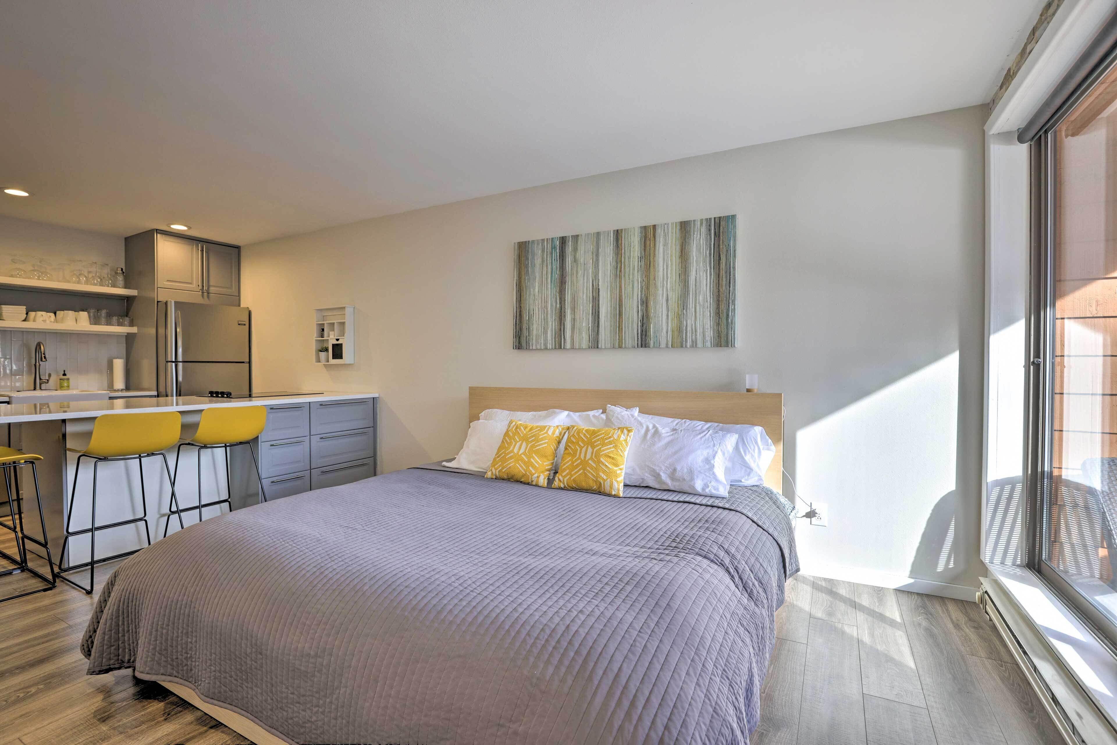 Una camera da letto moderna con un letto grande, un angolo cottura e una zona pranzo con sedie gialle.