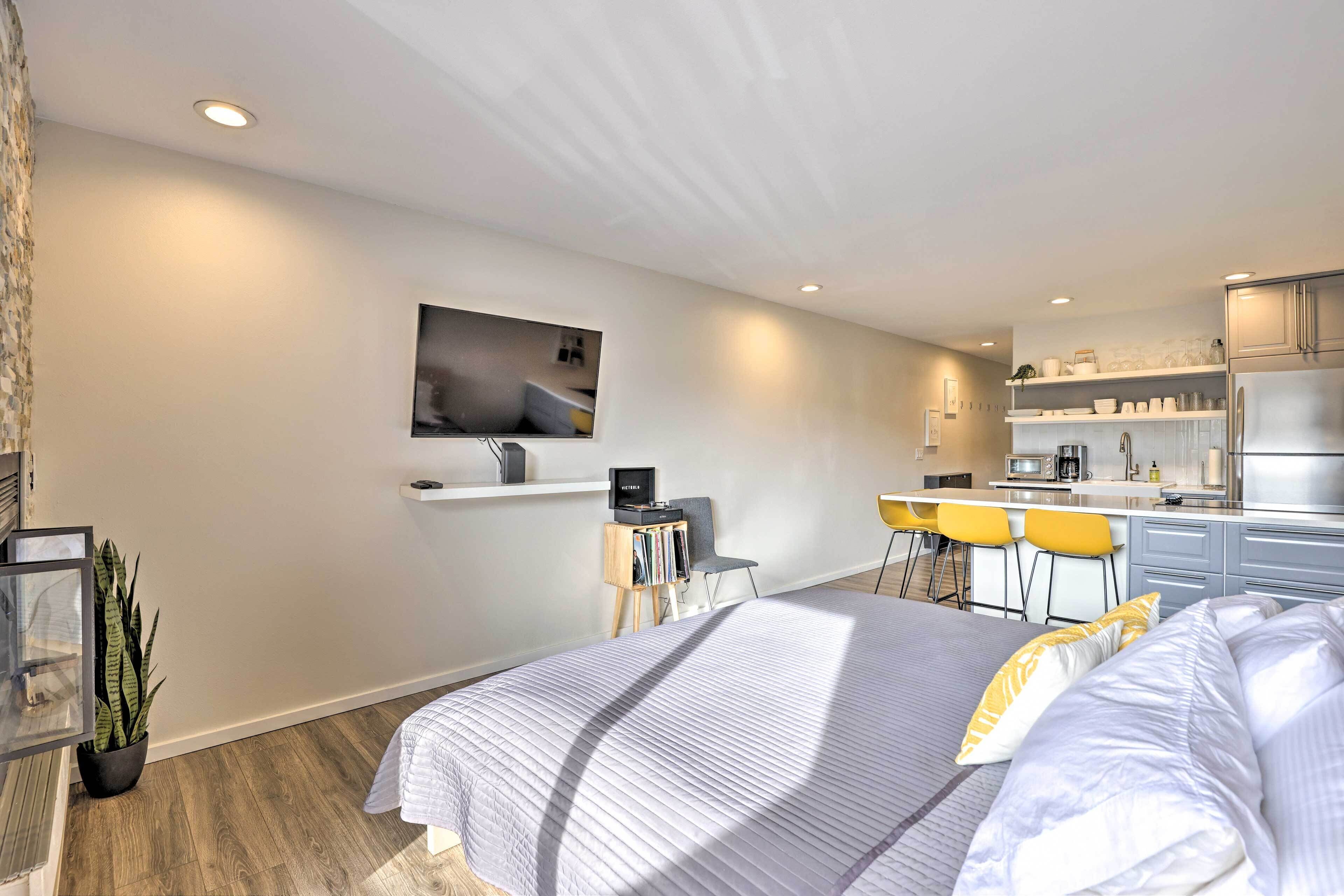 Un dormitorio moderno con una cama grande, un escritorio y una kitchenette al fondo.