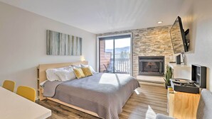 Un dormitorio moderno con cama, televisor, chimenea y balcón con vistas.