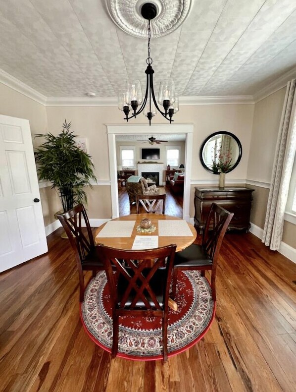 Une salle à manger avec une table ronde, des chaises en bois, un lustre et un tapis à motifs.