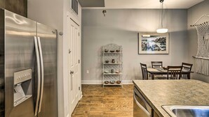 Una cocina moderna con un refrigerador de acero inoxidable, piso de madera, un área de comedor con una mesa y sillas, y un estante de pared con vajilla.