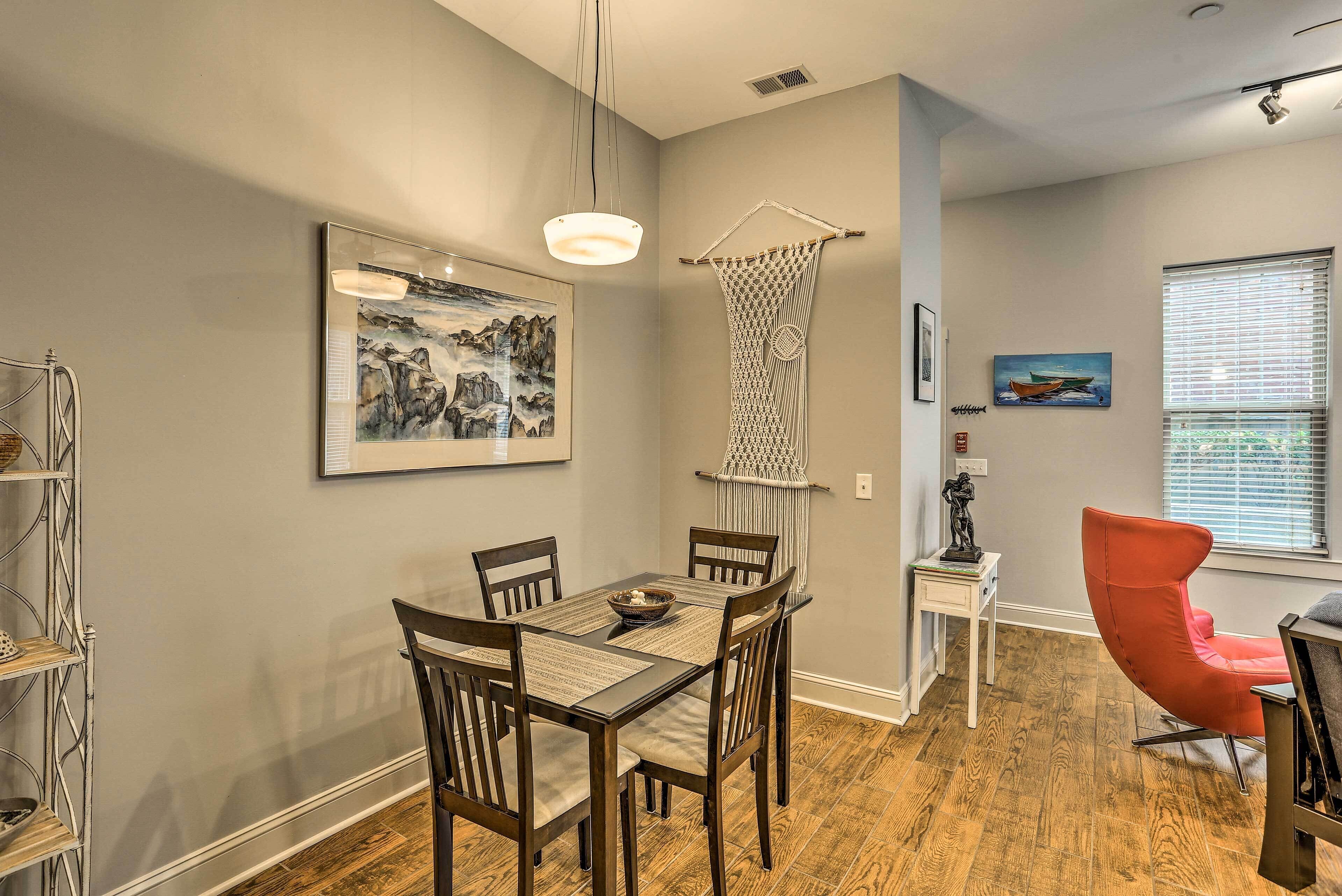 A dining area with a wooden table and chairs, a hanging light fixture, and artwork on the walls.