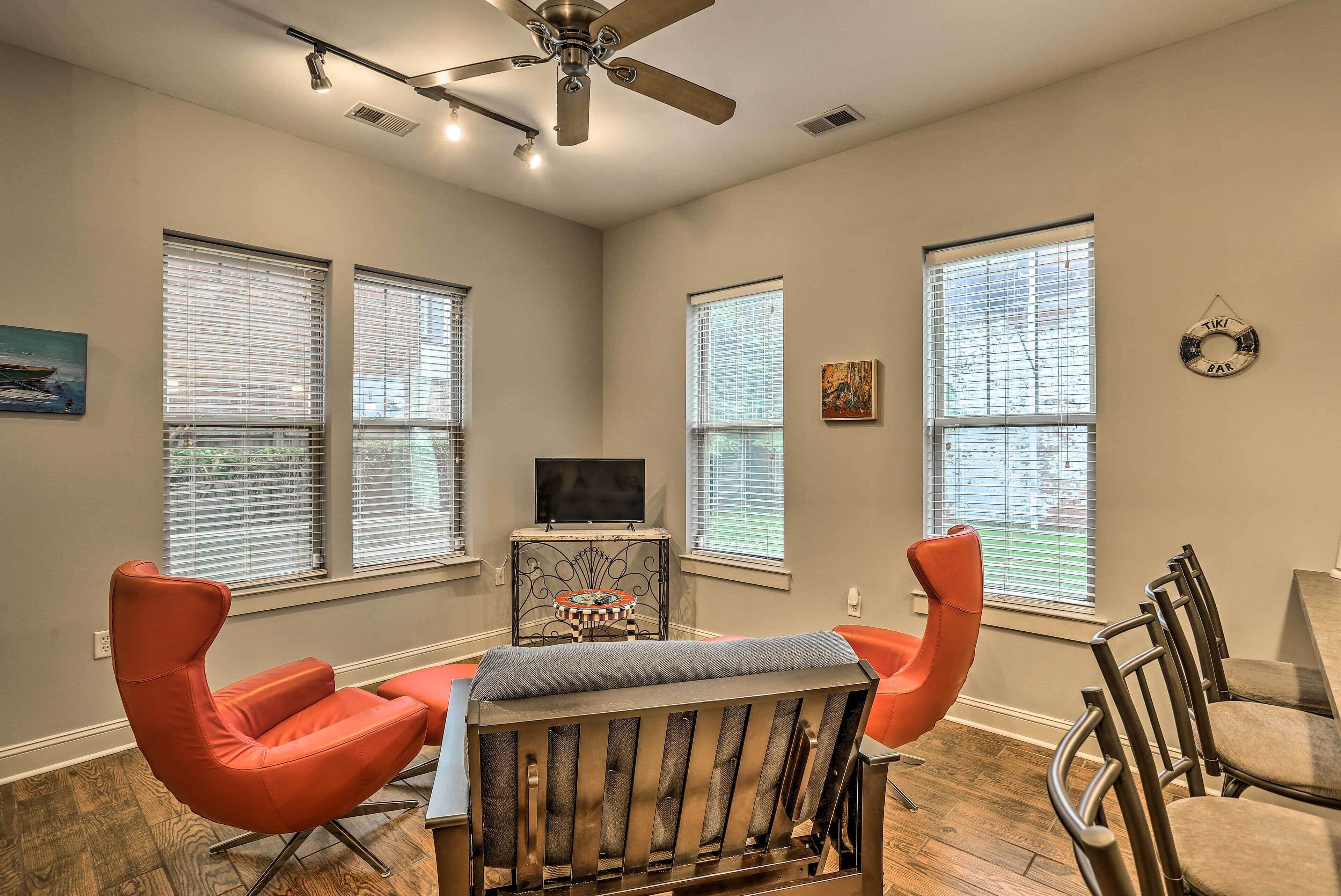 A dining area with a table and chairs, a ceiling fan, and large windows with blinds.