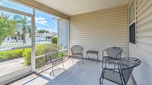 A covered patio with metal chairs and a small table, large windows offering a view of the neighborhood. - Sunny Home in The Villages w/ Lanai & Pool Access! (The Villages)