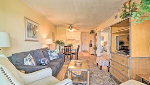 A living room with a sofa, coffee table, and a TV stand. There is a dining area with a table and chairs. - Walk to Beach! Isle of Palms Condo w/ Pool Access (Isle of Palms)