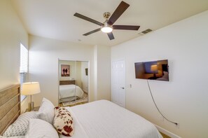 A hotel room with a bed, a ceiling fan, a television mounted on the wall, and a door leading to another room. - Bermuda Dunes Home w/ Private Pool, Patio & Grill! (Indio)