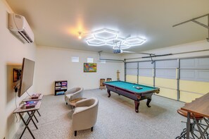 A pool table in a room with a ceiling-mounted projector, a pool cue rack, and a bookshelf with board games. - Bermuda Dunes Home w/ Private Pool, Patio & Grill! (Indio)