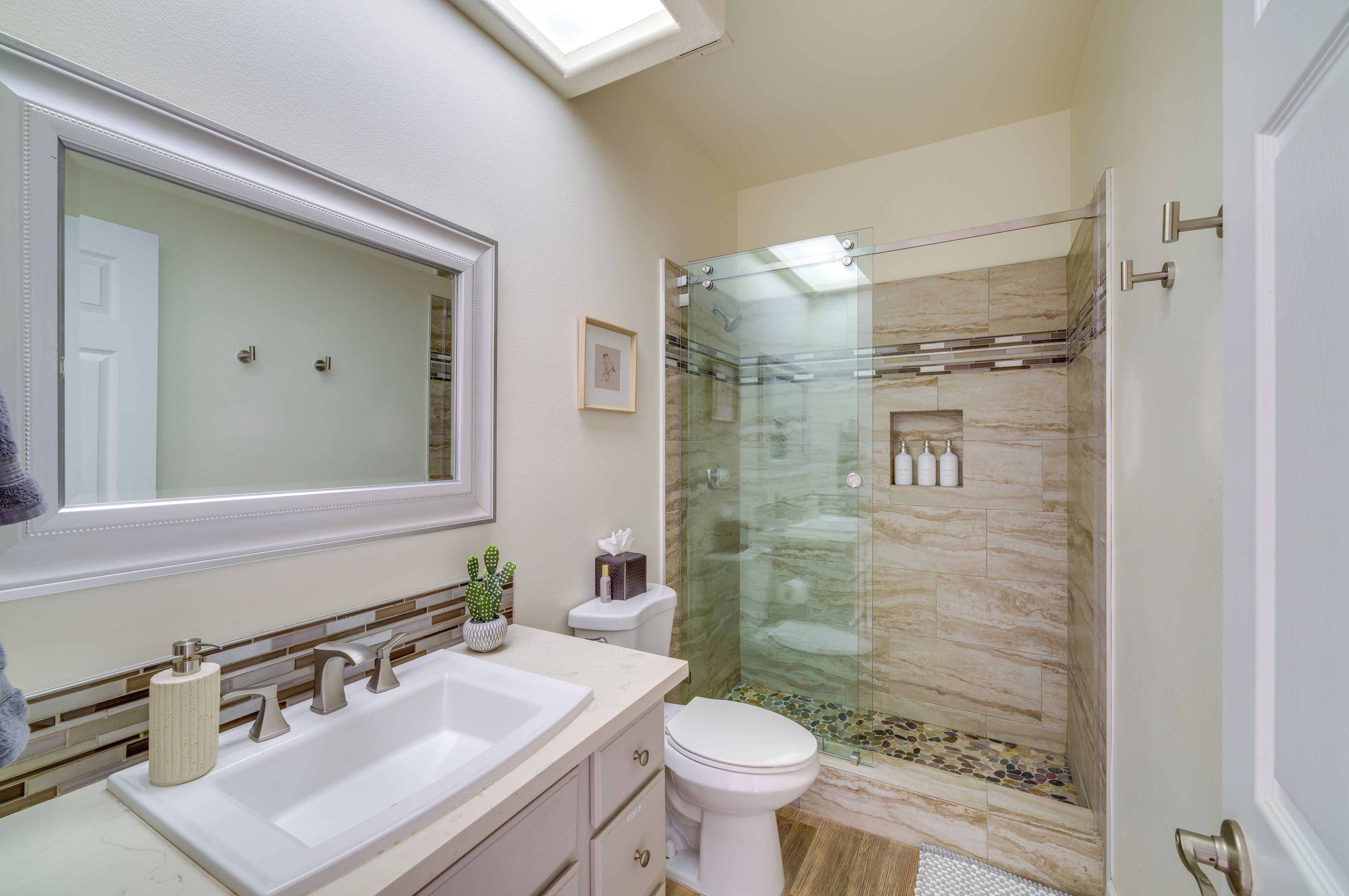 A bathroom with a glass-enclosed shower, a large mirror, and a sink with a vase of flowers.