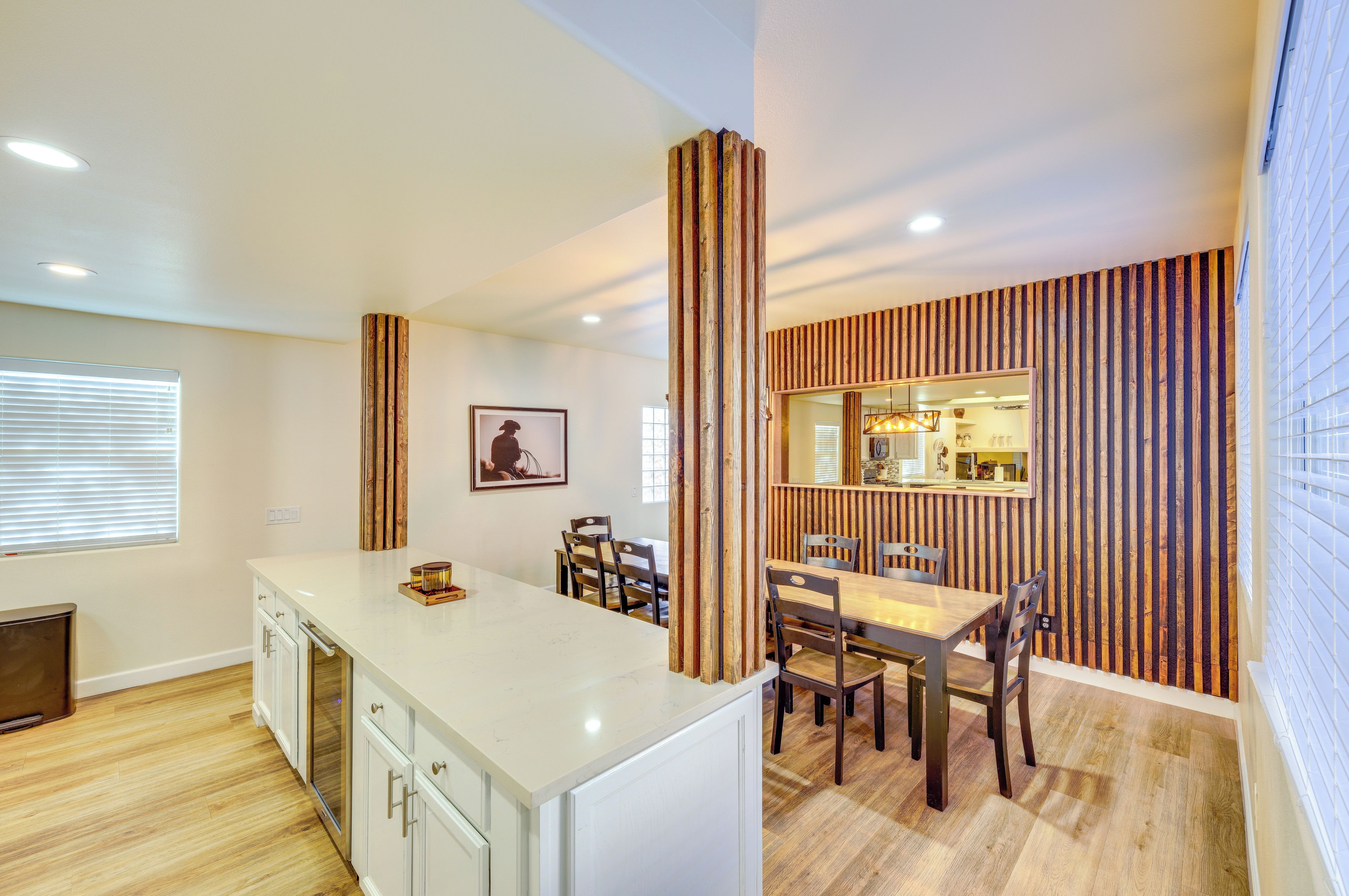 A modern kitchen with a white countertop, wooden chairs, and a dining table.