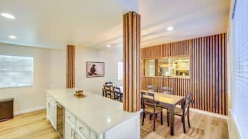 A modern kitchen with a white countertop, wooden chairs, and a dining table.