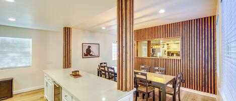 A modern kitchen with a white countertop, wooden chairs, and a dining table.