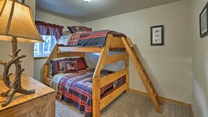 Un lit superposé avec une échelle en bois, une commode en bois avec une lampe et une fenêtre avec des rideaux.