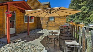Une cabane en bois dotée d’un patio comprenant une table, deux chaises, un grand parasol et un tonneau.