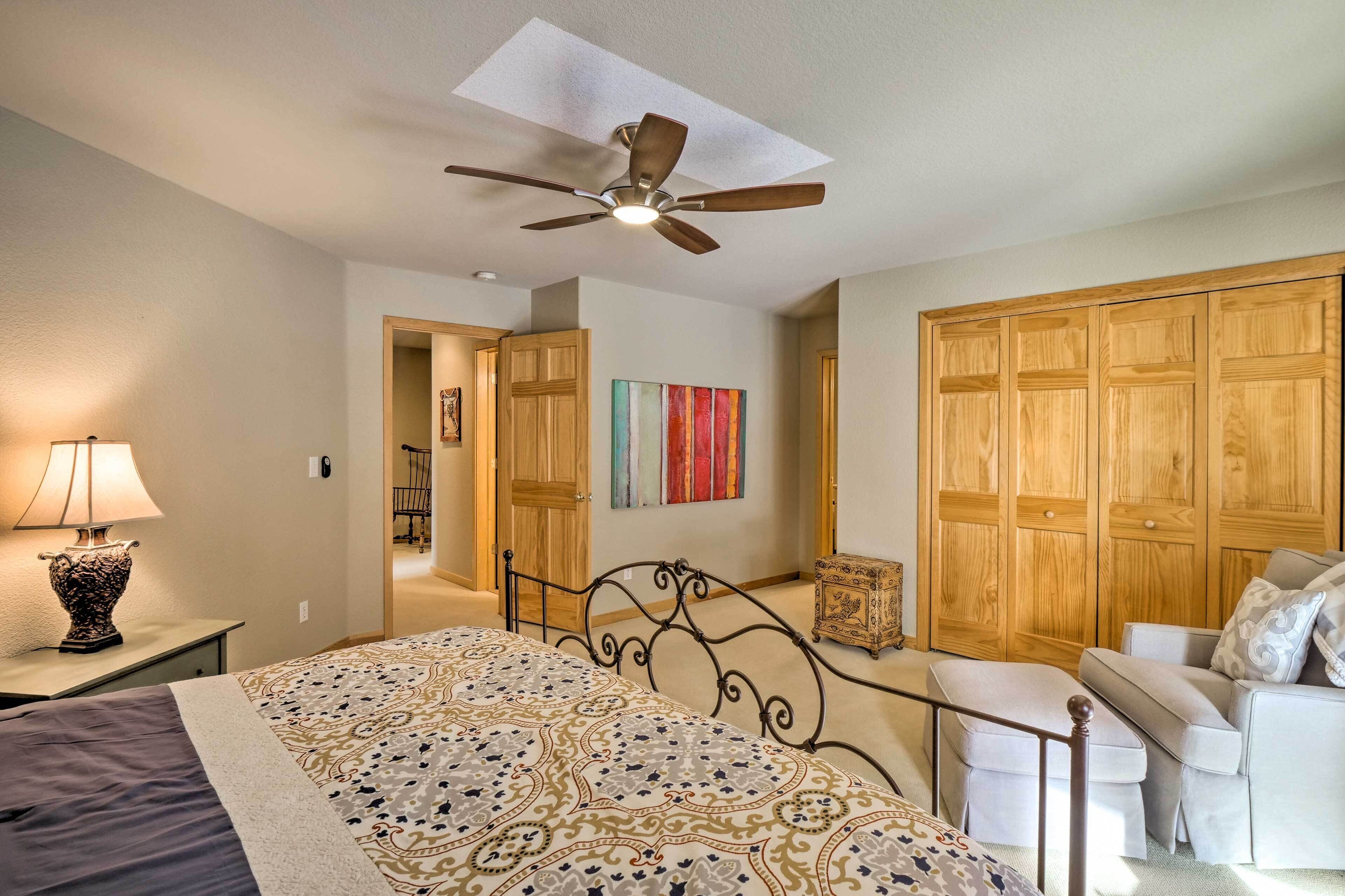 A bedroom with a bed, a ceiling fan, a nightstand, a lamp, a dresser, a chest of drawers, and a sofa.