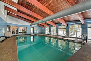 Un'ampia piscina coperta con travi in legno, ampie vetrate e una parete piastrellata.